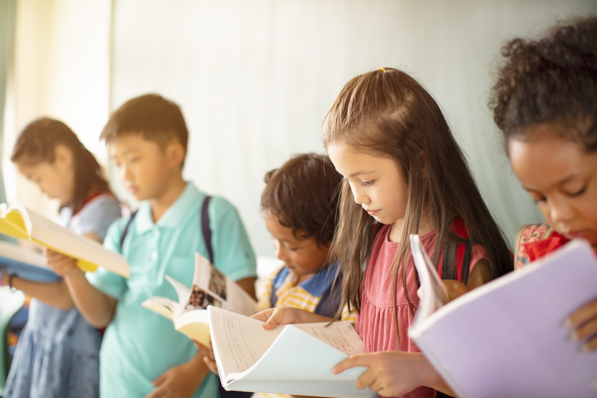 School children standing in a line reading books.