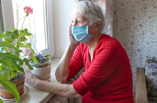 Old woman with a facemask looking out a window