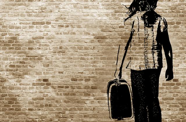 Graffiti/shadow on a brickwall showing a refugee girl walking with her suitcase