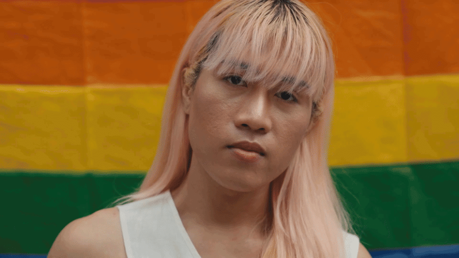 The video starts with a close up of a trans woman standing in front of a rainbow flag, looking in camera with a strong expression. The following video portrays a young man with down syndrome with his arms crossed. He is portrayed at work, in a flower farm. This is followed by a video of a young woman of African descent looking in camera while walking in a big city. The video is closed by footage of an elderly man in a park, wearing a hat, looking in camera.