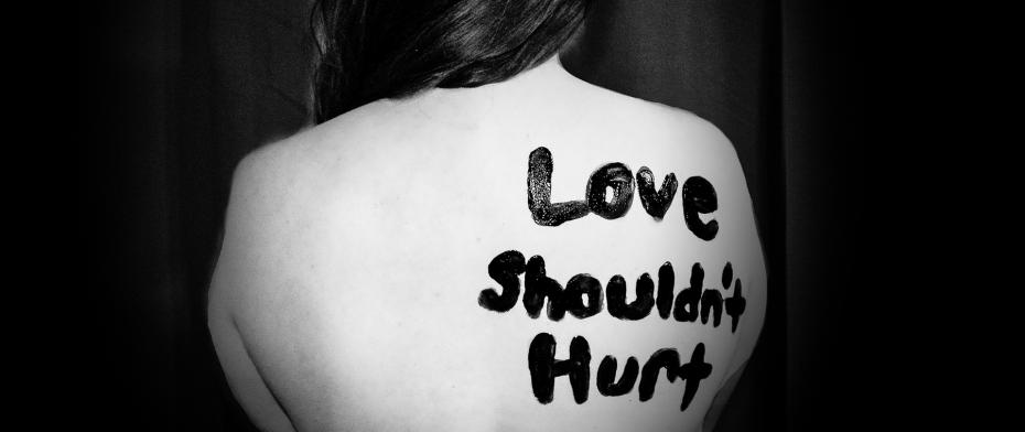 Woman's back with painted message: "Love Shouldn't Hurt." Black and white, advocating against abuse.