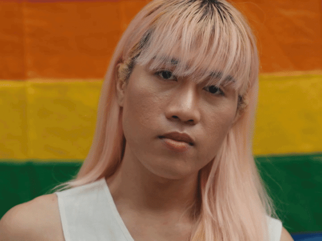 The video starts with a close up of a trans woman standing in front of a rainbow flag, looking in camera with a strong expression. The following video portrays a young man with down syndrome with his arms crossed. He is portrayed at work, in a flower farm. This is followed by a video of a young woman of African descent looking in camera while walking in a big city. The video is closed by footage of an elderly man in a park, wearing a hat, looking in camera.