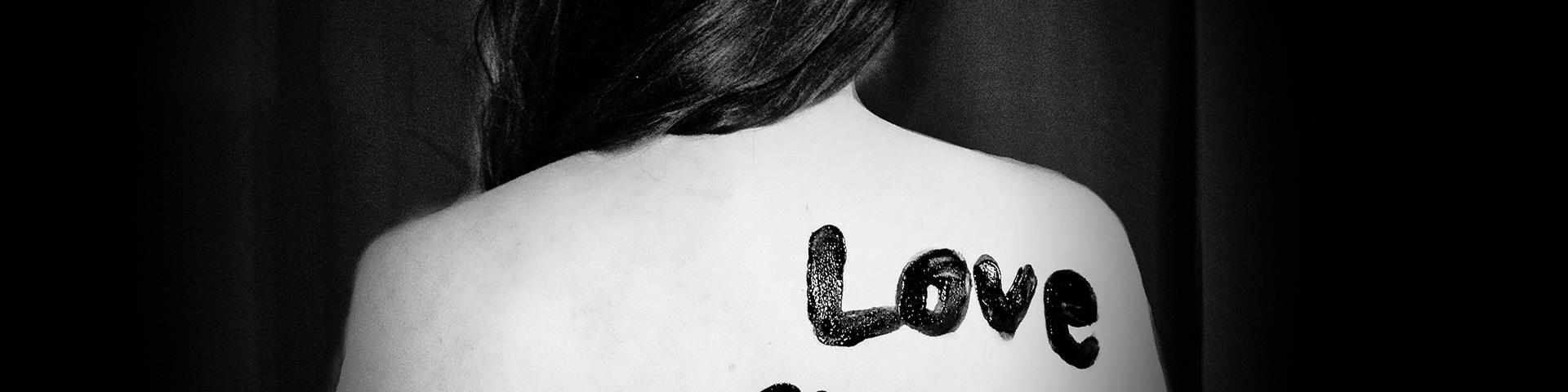 Woman's back with painted message: "Love Shouldn't Hurt." Black and white, advocating against abuse.